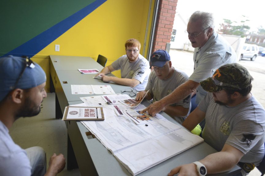 Architectural drafting students working on blueprints with instructor guidance.