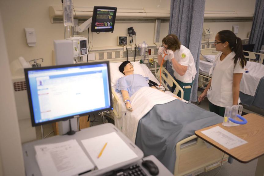 Nursing RN training simulation with students practicing patient care in hospital clinical skills lab.