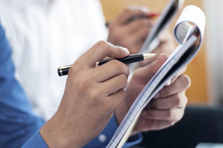 Student taking notes during journalism class with tablet and notebook.