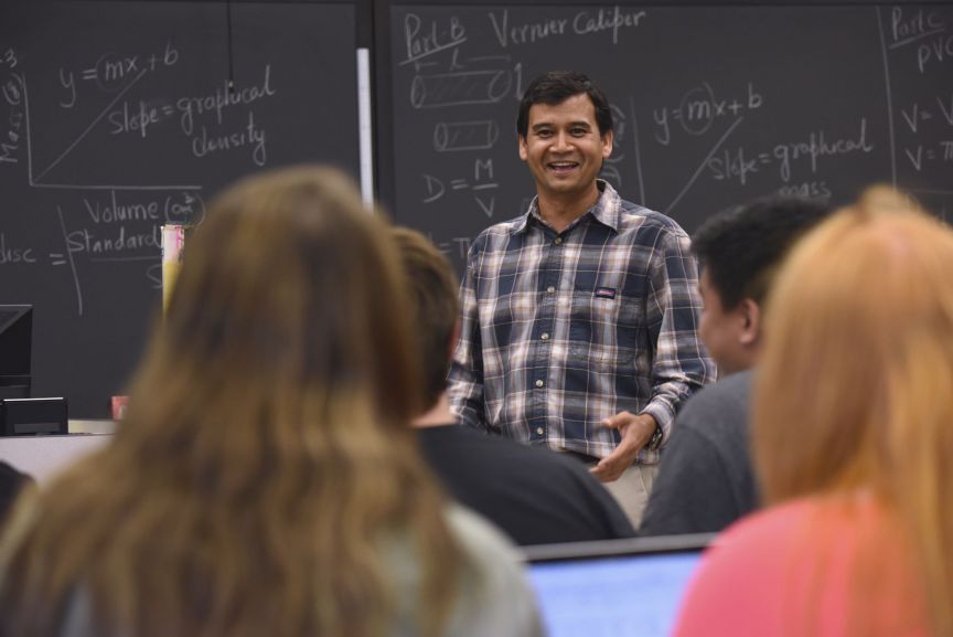 College instructor teaching students in classroom with blackboard background.