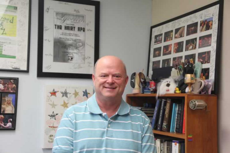 Theater director at Pensacola State College with Vietnam War-themed play background.