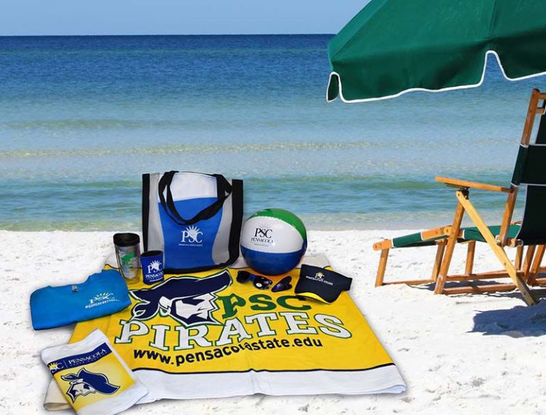 Beach gear with Pensacola State College branding, including a towel, bag, and volleyball, on a sunny beach with an umbrella. Pensacola State College beach gear with branded towel, bag, and volleyball on sunny Gulf Coast beach.