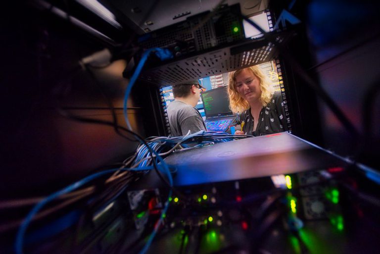 Cybersecurity students analyzing network data in a server room for higher education programs.