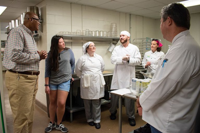 Chef Kevin Belton engaging with students and instructors in a professional kitchen setting.