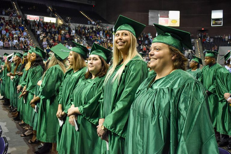 Graduates in green caps and gowns celebrating at Pensacola State College graduation ceremony.