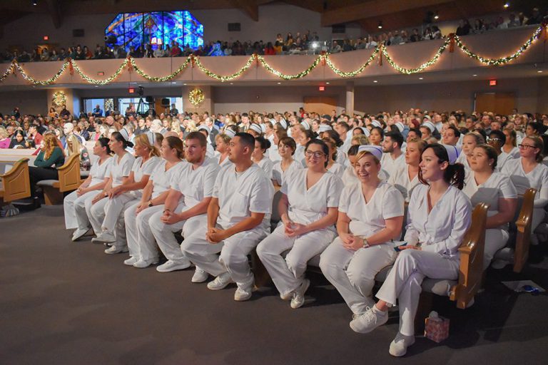Nursing students in white uniforms attending Pensacola State College pinning ceremony.