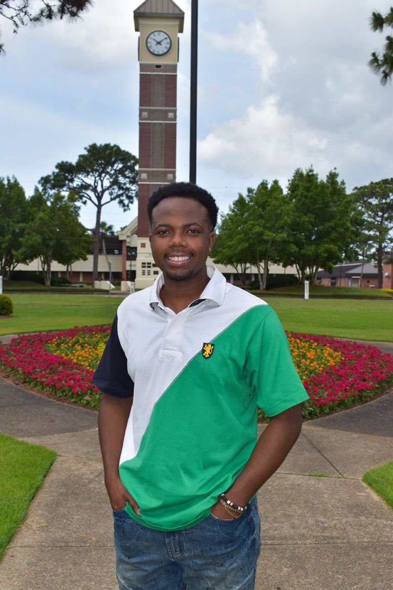 College student smiling outdoors at Pensacola State College campus with clock tower in background.