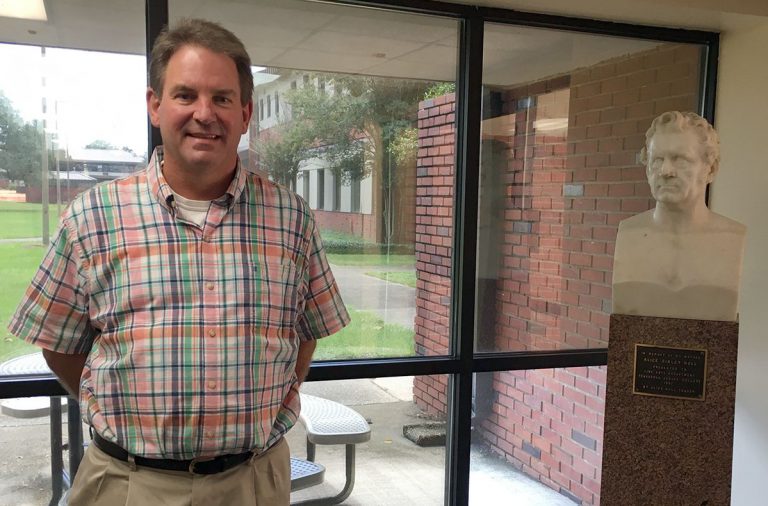 Kenneth Phillips, new Performing Arts Director, at Pensacola State College, standing beside a bust i.