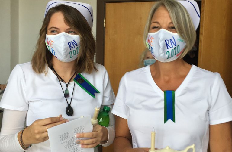 Two nursing graduates in masks and caps celebrating graduation at Pensacola State College.