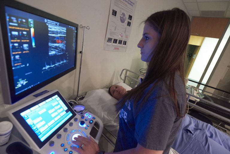 Ultrasound technician student practicing sonography skills on patient in educational setting.