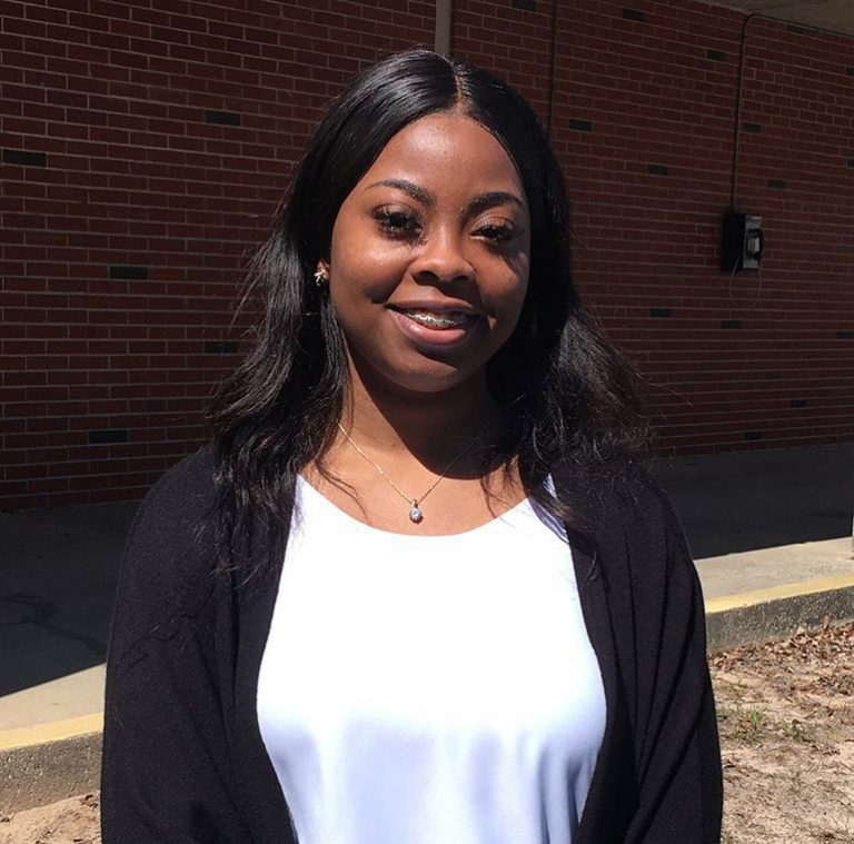 Student smiling outdoors at Pensacola State College campus.