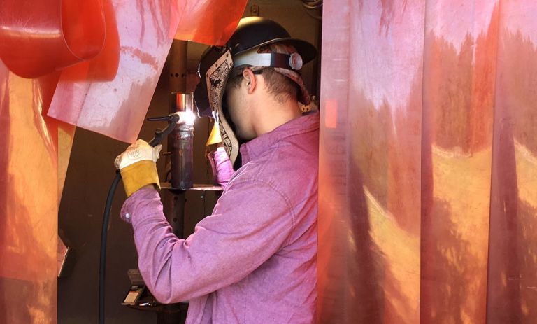 Welding student in safety gear working on metal project at PSC.