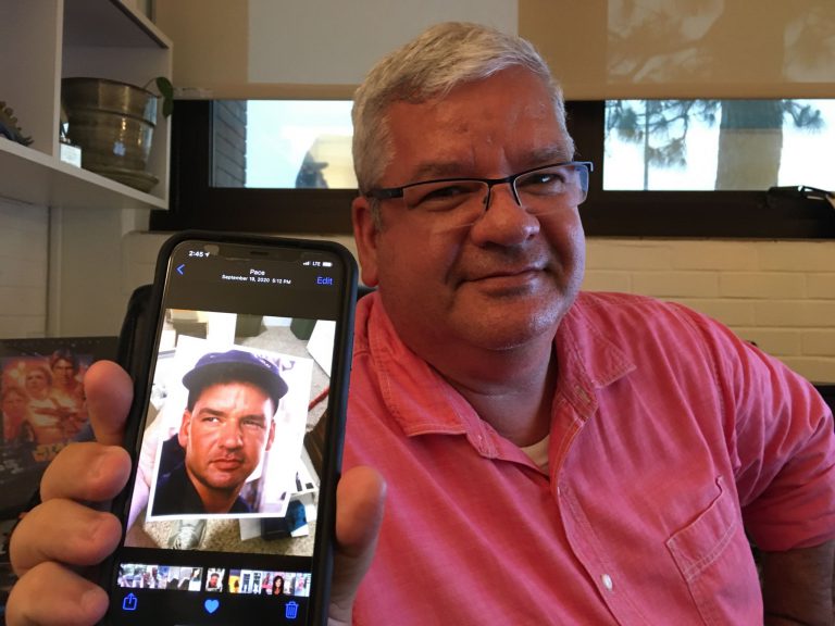 Jason King, PSC web administrator, holding a phone with Coast Guard Auxiliary member badge.