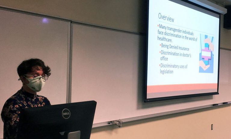Research student presenting healthcare discrimination topics at Pensacola State College classroom.