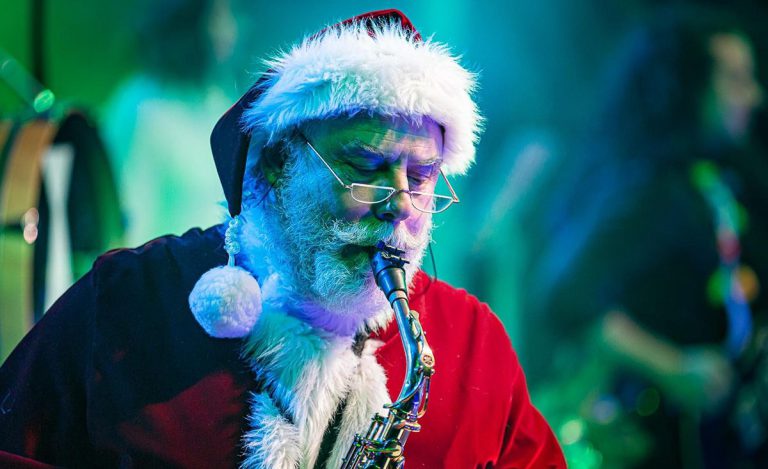 Festive Santa saxophonist at college holiday event Santa Claus playing saxophone during college holiday celebration.