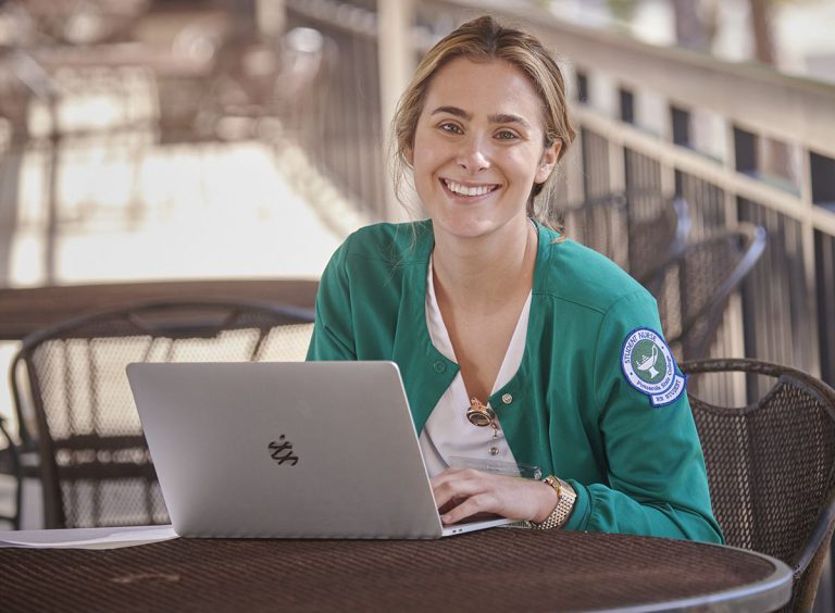 Pensacola State RN to BSN Program ranking boost Highly accessible image of a smiling nursing student with laptop outdoors.
