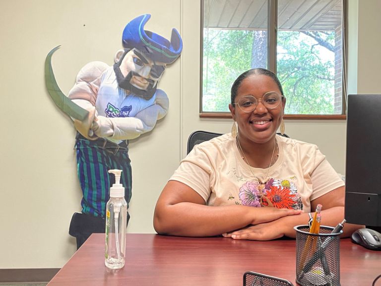 College adviser Tyra Henderson at desk with mascot in office, promoting student support services.