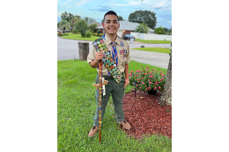 Eagle Scout Nicolas Salazar in Boy Scout uniform holding a decorated staff outdoors.
