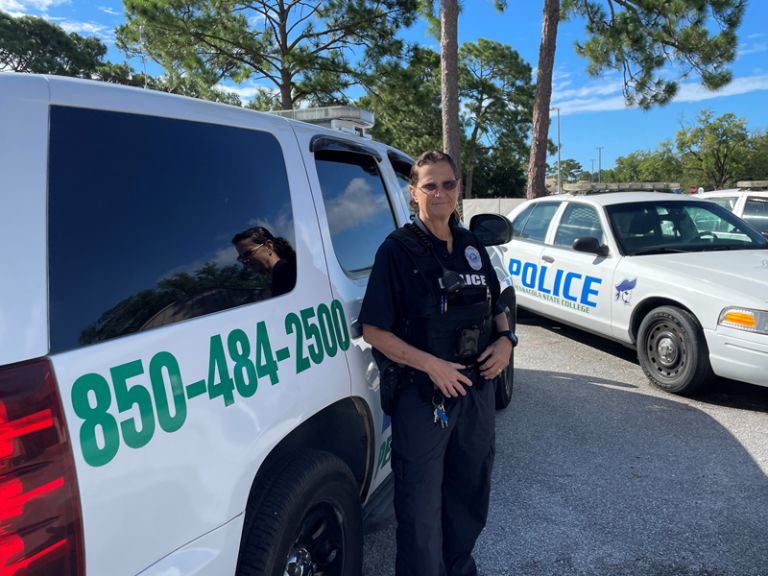 Police officer Kim Cooper in uniform with police vehicles at Pensacola State College.