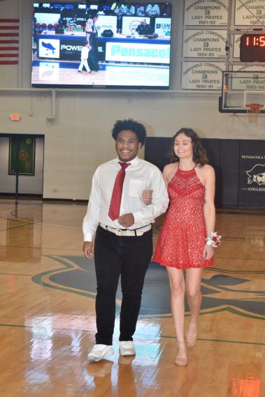 Young man and woman dressed in formal attire on basketball court during homecoming event.