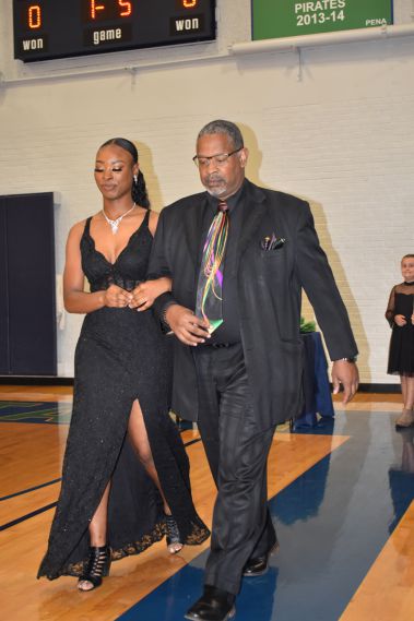 Elegant young woman in black gown and man in suit at college event.