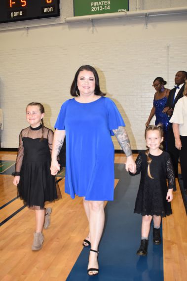 Smiling woman in blue dress walking with two young girls during homecoming event.