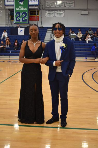 Elegant young woman in formal black gown and man in blue suit at Homecoming event.