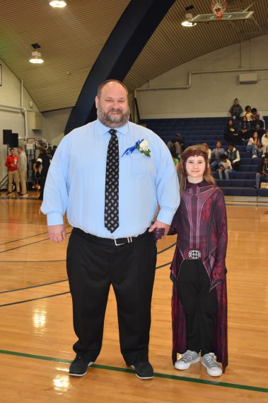 Smiling man and young woman at homecoming event in gymnasium.
