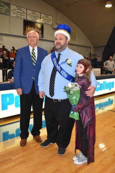 Man wearing a blue graduation cap and sash with a young girl holding flowers.