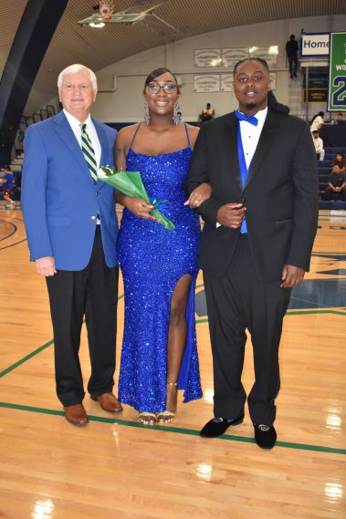 Senior student in formal attire with faculty member and fellow student.