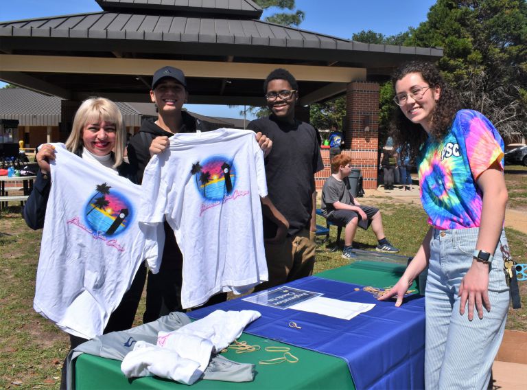 Celebrating Pirate Fest 2023 with PSC family members holding themed T-shirts outdoors.