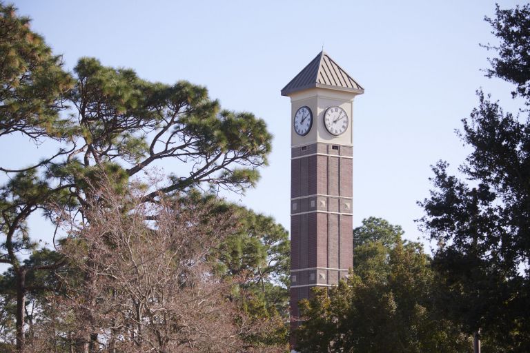 Campus Clock Tower at Pensacola State College, Florida, with trees and clear sky. Clock tower on Pensacola State College campus, Florida, surrounded by trees.