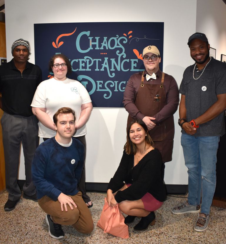 Diverse group of students showcasing graphic design projects at PSC student exhibition.