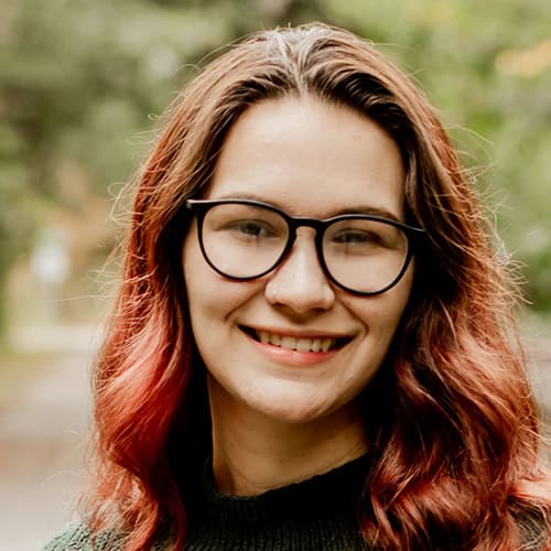 Jessica Anderson smiling outdoors, wearing glasses, promoting higher education at Pensacola State College. Jessica Anderson, college student with glasses, smiling outdoors, representing higher education at P.