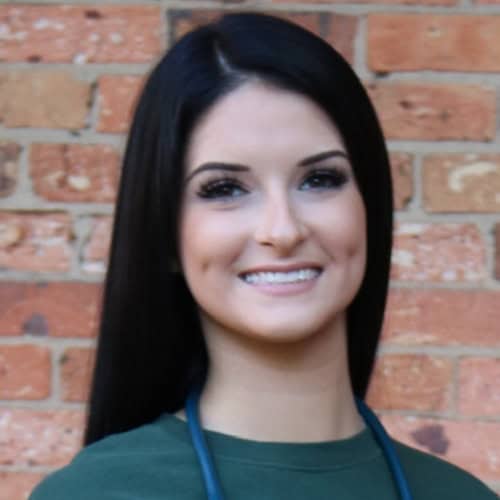Kelsey Ratzin at Pensacola State College campus Portrait of Kelsey Ratzin, a student at Pensacola State College, smiling against a brick wall backgr.