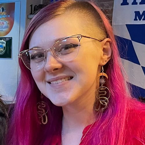 Morgan Joiner smiling with pink hair and glasses, showcasing her unique style at Pensacola State College event. Morgan Joiner with pink hair, glasses, and statement earrings at Pensacola State College event.