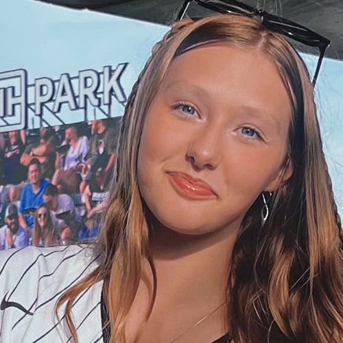 Shelby Smith at Pensacola State College campus event Young woman with long red hair, smiling, wearing sunglasses on her head, at college event.