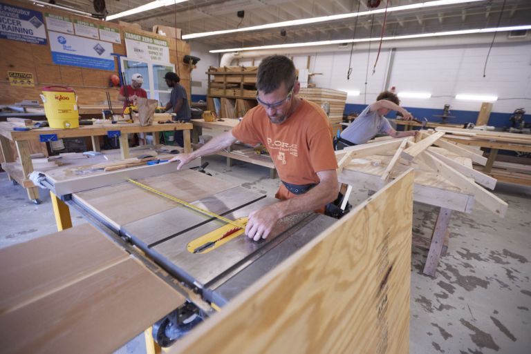 Woodworking student using a table saw in a college workshop for technical education.