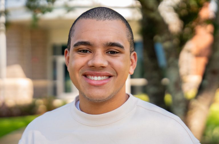 Diverse student smiling outdoors at Pensacola State College campus, highlighting higher education op.