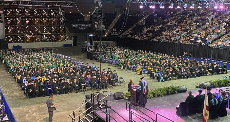 Pensacola State College graduation ceremony with graduates in caps and gowns on stage.