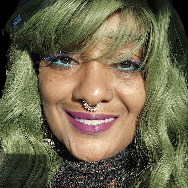 Empowered woman with green hair and vibrant makeup at Pensacola State College event Empowered woman with green hair, colorful makeup, and jewelry smiling at Pensacola State College eve.