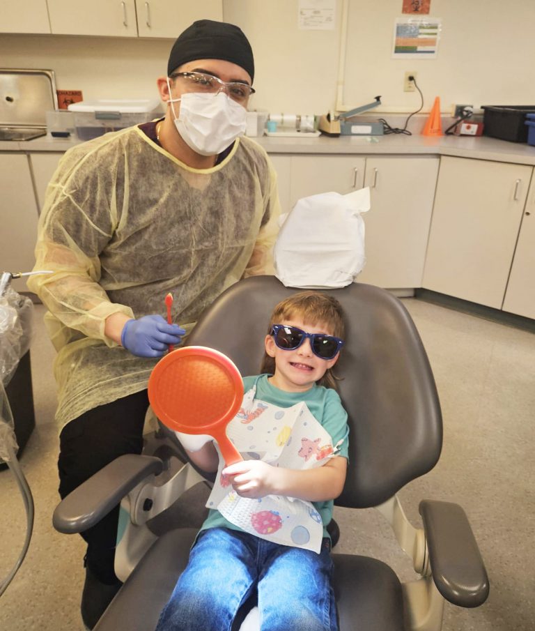 Dental hygiene student providing dental care to a smiling child at Pensacola State College clinic.