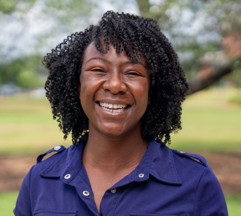 Alumni smiling outdoors in a blue uniform, representing higher education achievement and community i.