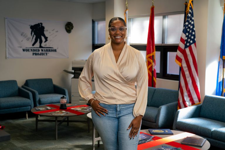 Veteran student at PSC with flags and Wounded Warrior Project banner in background.
