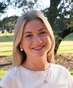 College student smiling outdoors on campus with trees in the background.
